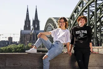 Studenten der PIXL VISN media arts academy posieren vor der Deutzer Brücke mit dem Kölner Dom im Hintergrund